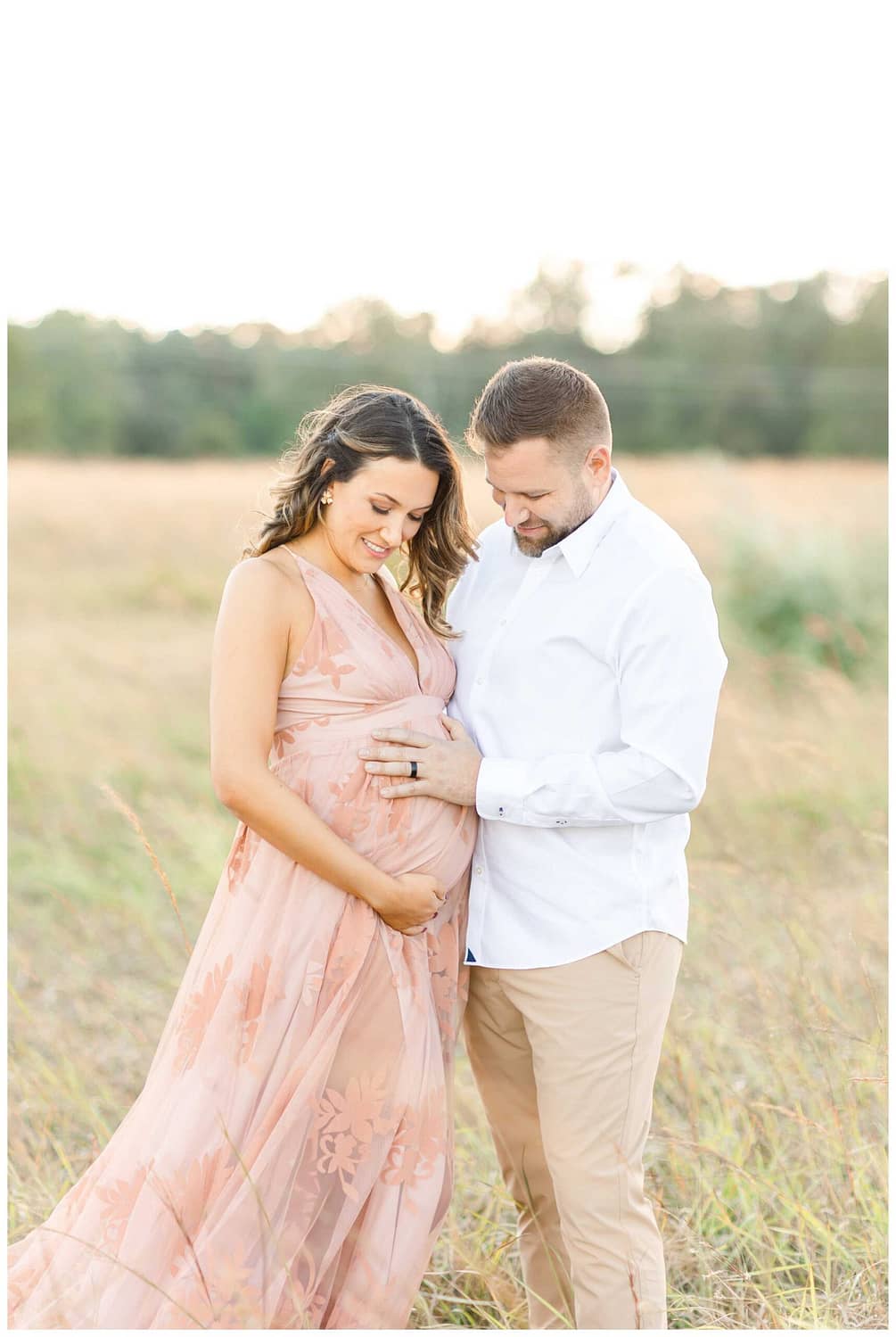 A pregnant mother and her husband holding their pregnant belly outside in a field looking down at the belly by Maternity Photographer DC